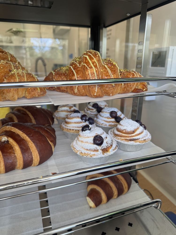 Croissants, cream buns and pastries on chrome shelves behind the display glass